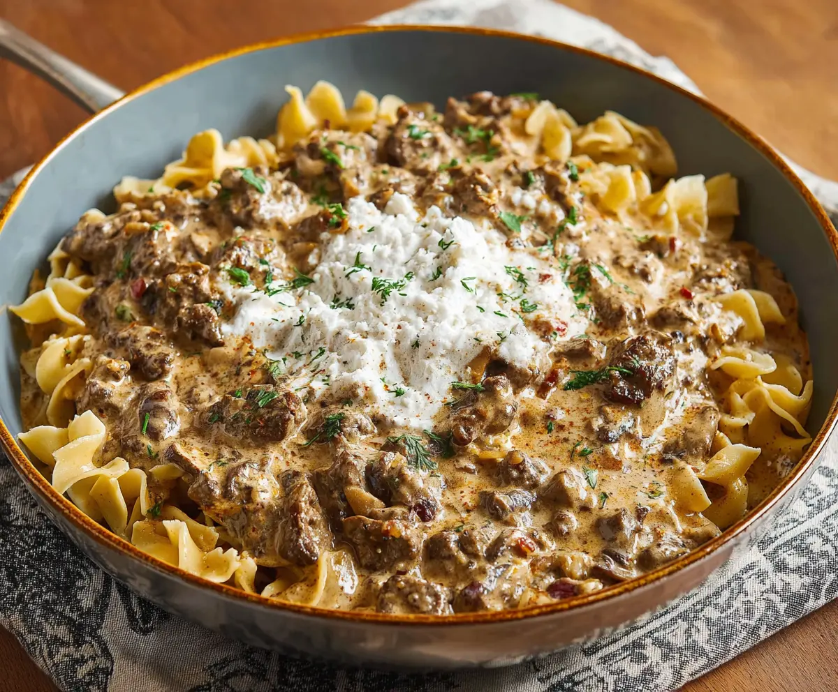 Creamy beef stroganoff served over noodles with fresh herbs, perfect for a comforting dinner.